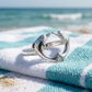 Dolphin heart ring resting on a beach towel