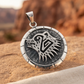 Round sterling silver bear-head pendant on sandstone with desert cliffs softly blurred behind.